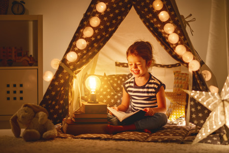 happy child girl laughing and reading book in dark in a tent at home
の写真素材