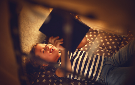 happy child girl laughing and reading book in dark in a tent at home
の写真素材