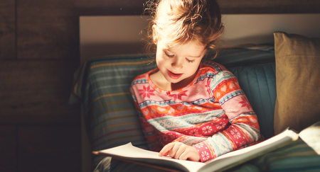 girl child reads book in bed before bedtimeの写真素材
