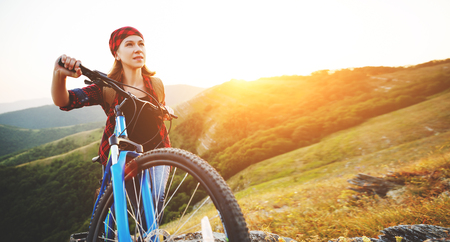 Woman tourist on a bicycle at the top of the mountain at sunset outdoors during a hike in summerの写真素材