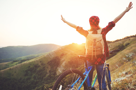 Woman tourist on a bicycle at the top of the mountain at sunset outdoors during a hike in summerの写真素材