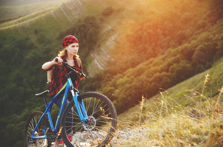 Woman tourist on a bicycle at the top of the mountain at sunset outdoors during a hike in summerの写真素材