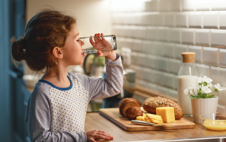 child girl is drinking water in the kitchen at homeの写真素材