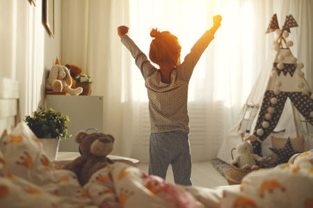 child girl wakes up in morning in bed and stretches by window
の写真素材