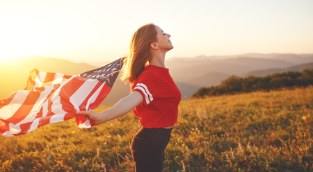 young happy woman with flag of united states enjoying the sunset on natureの写真素材