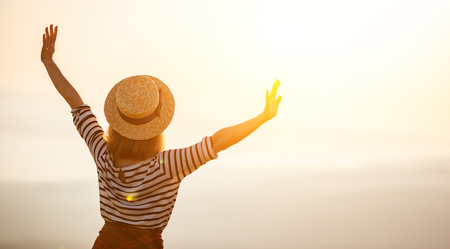 Happy woman jumping and enjoying life in field at sunset in mountainsの写真素材
