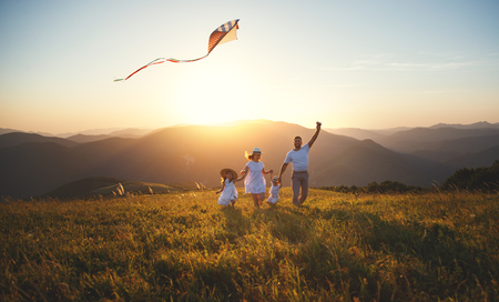 Happy family father,  mother and children launch a kite on nature at sunsetの写真素材