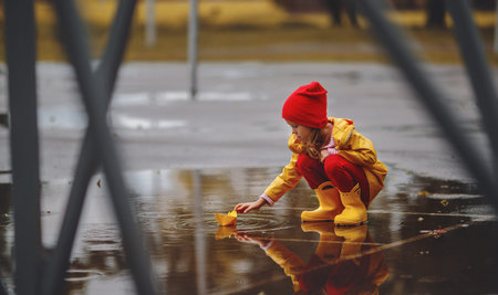 happy child girl with umbrella and paper boat in a puddle in   autumn on nature