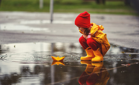 happy child girl with umbrella and paper boat in a puddle in   autumn on natureの写真素材