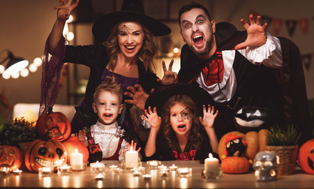 happy family mother father and children in costumes and makeup on a celebration of Halloween in dark homeの写真素材