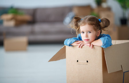 sad child girl sitting in box for moving to a new apartment