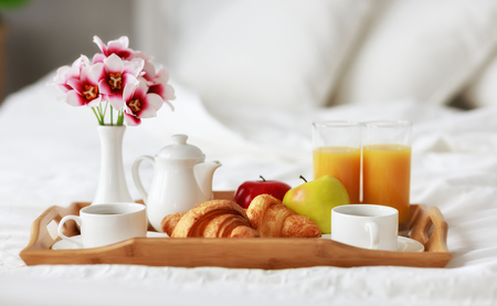 breakfast in bed of coffee, croissants, orange juice and fruit on a trayの写真素材