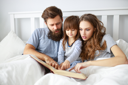 happy family mother, father and  father child daughter read a book, a fairy tale in bedの写真素材