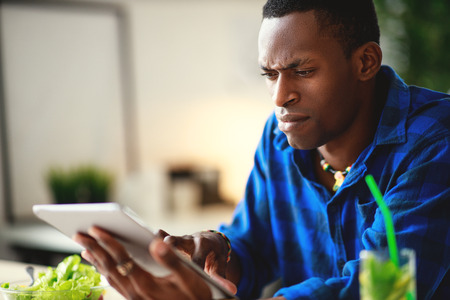 healthy eating. happy young black man eating salad with phone and tablet pc in the morningの写真素材