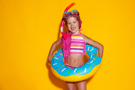Happy child girl in swimsuit with swimming ring donut on a colored yellow backgroundの写真素材