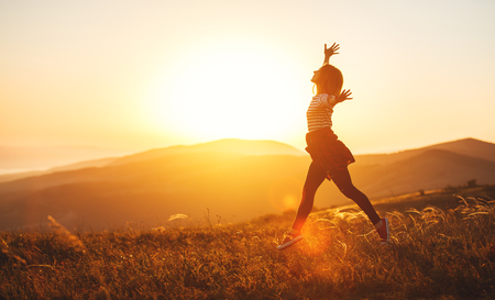 Happy woman jumping and enjoying life in field at sunset in mountainsの写真素材