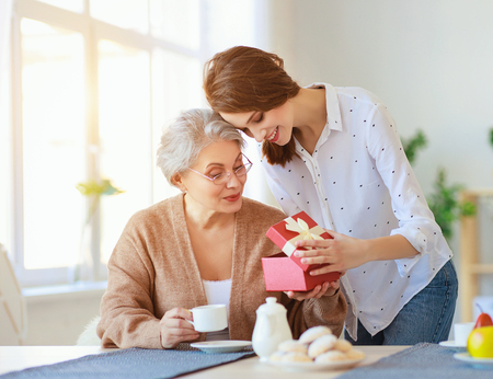 Happy mother's day! An adult daughter gives gift and congratulates an elderly mother on the holidayの写真素材