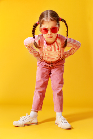 The funny funny child girl in pink clothes on yellow backgroundの写真素材