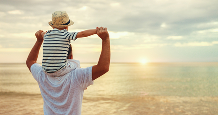 Father's day. Dad and baby son playing together outdoors on a summer beachの写真素材