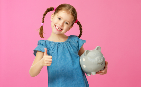 Financial concept of children's pocket money. A child girl with piggy bank on a colored pink backgroundの写真素材