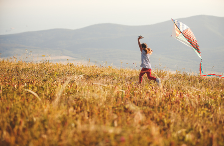 Happy child girl running with a kite at sunset outdoorsの写真素材
