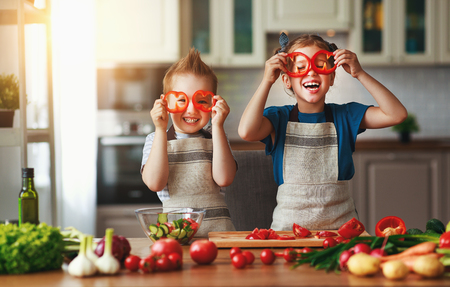 Healthy eating. Happy children prepares and eats vegetable salad in kitchenの写真素材