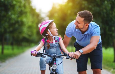 Happy family father teaches child daughter to ride a bike in the Park in natureの写真素材