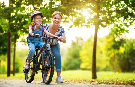 happy family mother teaches child daughter to ride a bike in the Park in natureの写真素材
