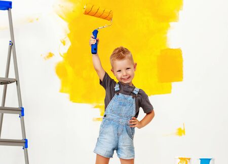 Repair in the apartment. Happy child boy paints the wall with yellow paintの写真素材