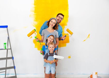 Repair in the apartment. Happy family mother, father  and children   paints the wall with yellow paint
の写真素材