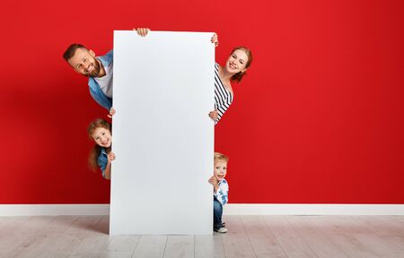 happy family mother father and children daughter and son  near an empty red wall with a white blank posterの写真素材