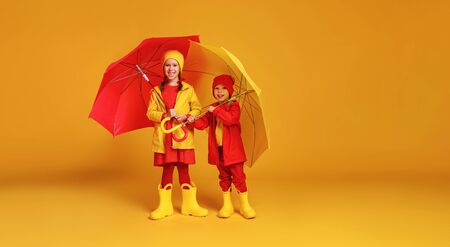 young happy emotional cheerful children friends laughing  with red umbrella   on colored yellow backgroundの写真素材