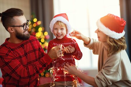happy family decorate Christmas tree, parents play with child son  with garlands at homeの写真素材