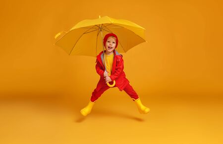 young happy emotional cheerful child boy jumping and laughing  with red umbrella   on colored yellow backgroundの写真素材