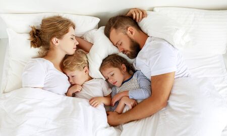 healthy sleep. happy family parents and children sleeping in white bed at homeの写真素材