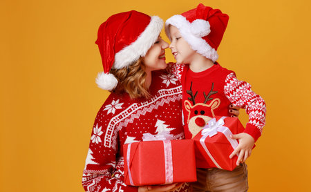 happy family mother and child son with christmas gifts and hats on yellow backgroundの写真素材