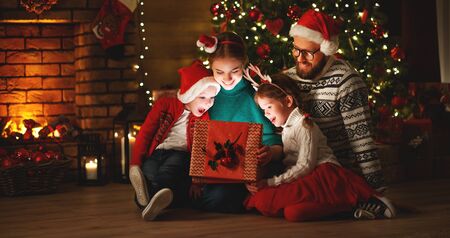 Merry Christmas! happy family mother father and children with magic gift near tree at evening at homeの写真素材