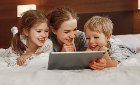 happy family mother and children with tablet computer at home in bed in the evening