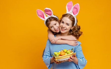 Happy easter! family mother and child daughter with ears hare getting ready for holiday on colored...