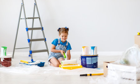renovation in the apartment. Happy child girl  paints the wall with yellow paint