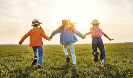 Unrecognizable cheerful little girls in casual clothes having fun and running back in together in...