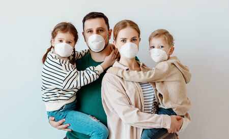 Parents and kids in medical masks looking at camera while standing against gray wall during contagious coronavirus epidemicの写真素材