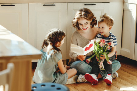 Smiling young woman reading greeting card while sitting on floor with cheerful little siblings with...