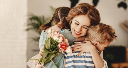 Happy Mothers Day! Children boy and girl congratulate smiling mother, hugs her  and give her flowers   bouquet of tulips during holiday celebration in kitchen at home
の写真素材