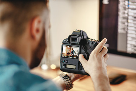 Back view of crop male photographer watching photos on display of professional camera while working...