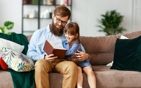 happy family. father hugs his little daughter and reads a book to her in the cozy living room of the houseの写真素材