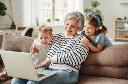 Cheerful senior female enjoying time with little grandchildren while sitting together on sofa and...