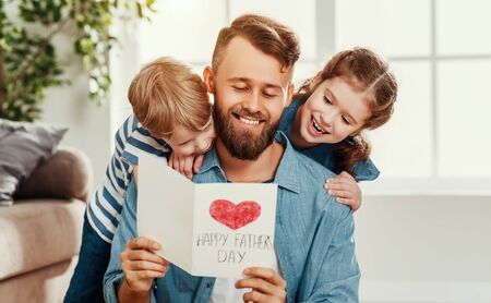 Cheerful little boy and girl congratulating happy dad with Fathers day and giving handmade greeting card while spending holiday together at homeの写真素材