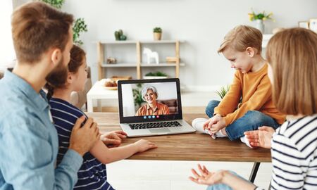 Modern parents and children sitting at table and speaking with elderly woman through video chat app on laptop while spending time at home together
の写真素材