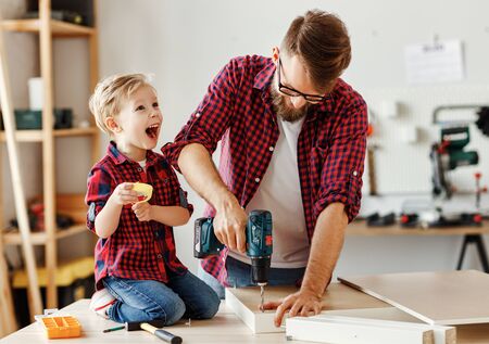 Excited little boy and young father in similar shirts holding drill together while working with wood in modern handicraft studioの写真素材